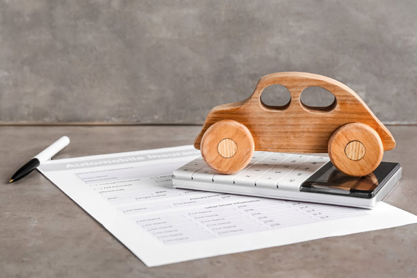 Ein hölzernes Spielzeugauto steht auf einem Taschenrechner, daneben liegt ein Blatt mit Tabellen.